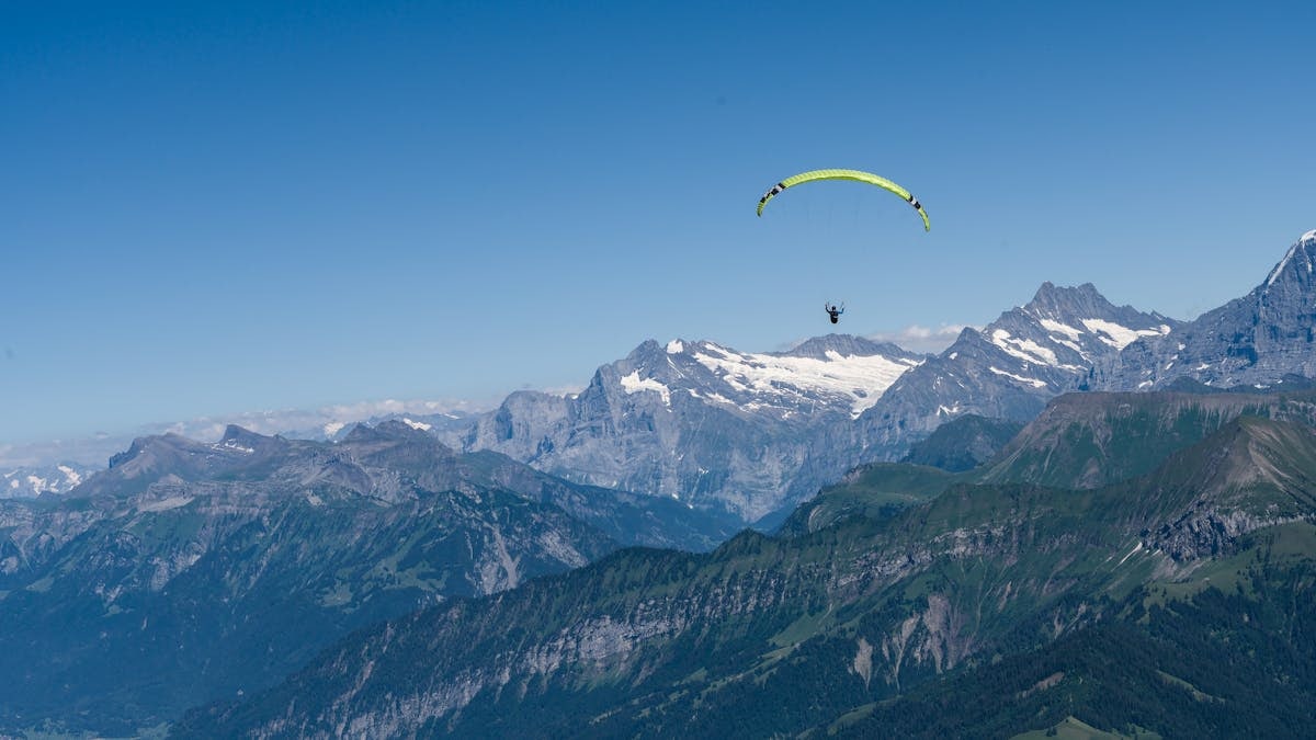 A paraglider soaring above the picturesque Swiss Alps with clear blue skies and stunning mountain views.